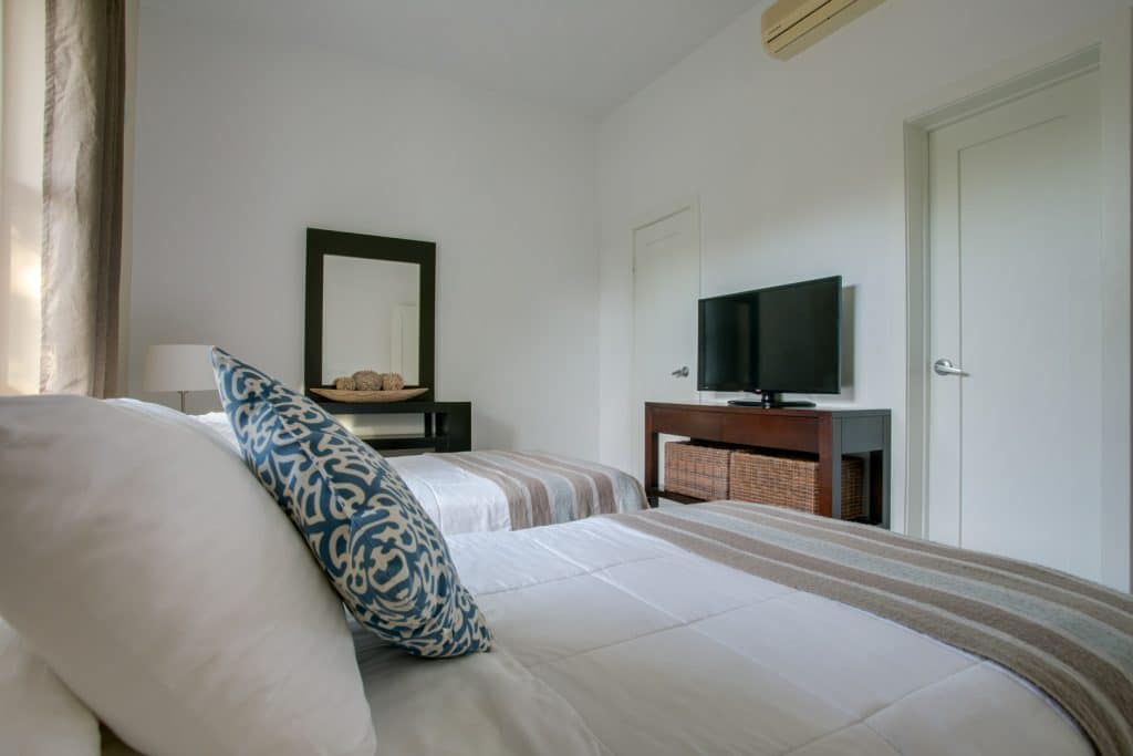 Corner view of the guest bedroom showing two queen sized beds with pillows and linen, a mirror and a television inside the 2 Bedroom Penthouse Lagoon Bayview at Umaya Resort & Adventure