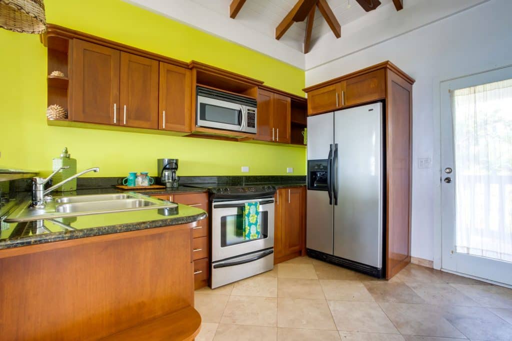 A kitchen with a stove, microwave, refrigerator, sink and a wooden cabinet with a black counter top inside the 1 Bedroom Beachfront at Umaya Resort & Adventure