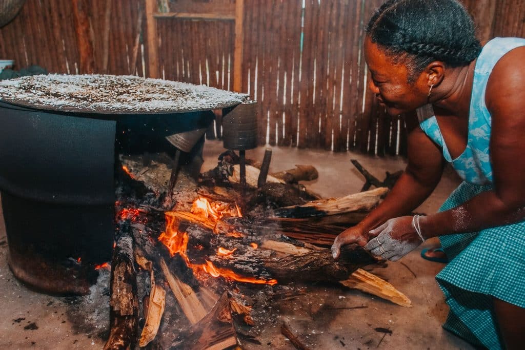 A garinagu woman feeding wood to the fire hearth where she is drying cassava on the comal during the Garifuna Cooking Class at The Lodge at Jaguar Reef