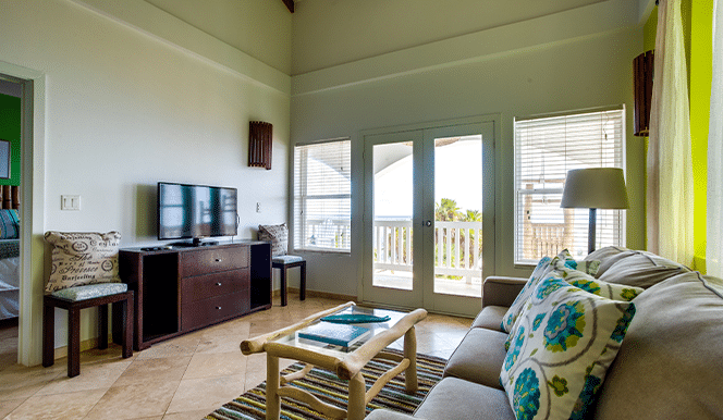 Living room area with a large grey couch, television, glass coffee table and a standing lamp inside the 2 Bedroom Penthouse Beachfront at Umaya Resort & Adventure