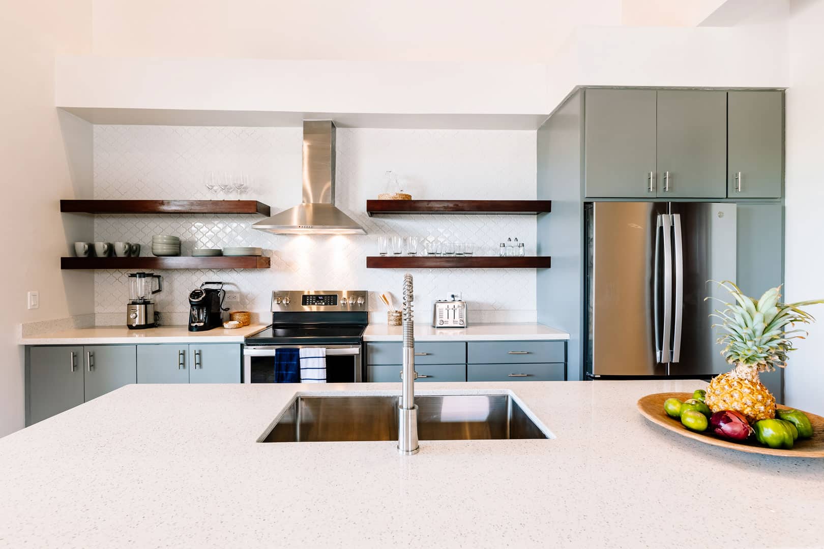 Kitchen area with sink, stove, refrigerator and fruits on the counter inside the 2 Bedroom Penthouse with Plunge Pool at The Lodge at Jaguar Reef Resort