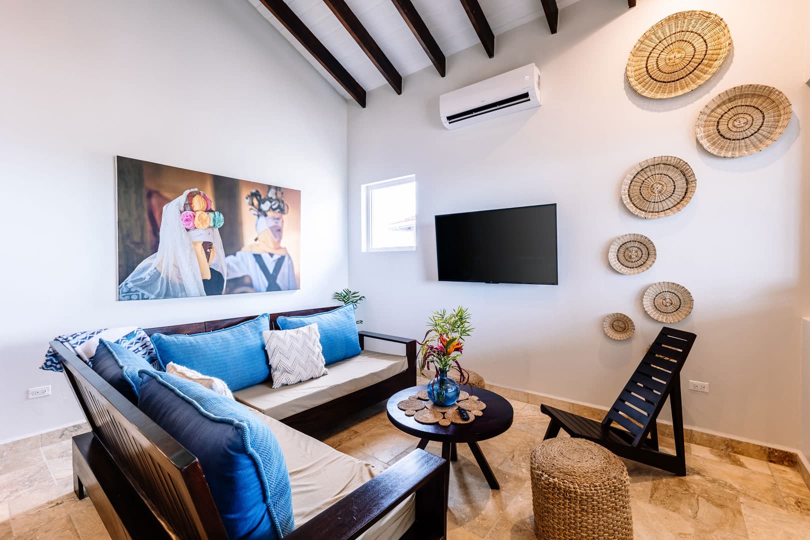 Living room area with an L shaped couch with pillows, a television on the wall and a folding beach chair and center table inside of the 2 Bedroom Penthouse with Plunge Pool at The Lodge at Jaguar Reef Resort