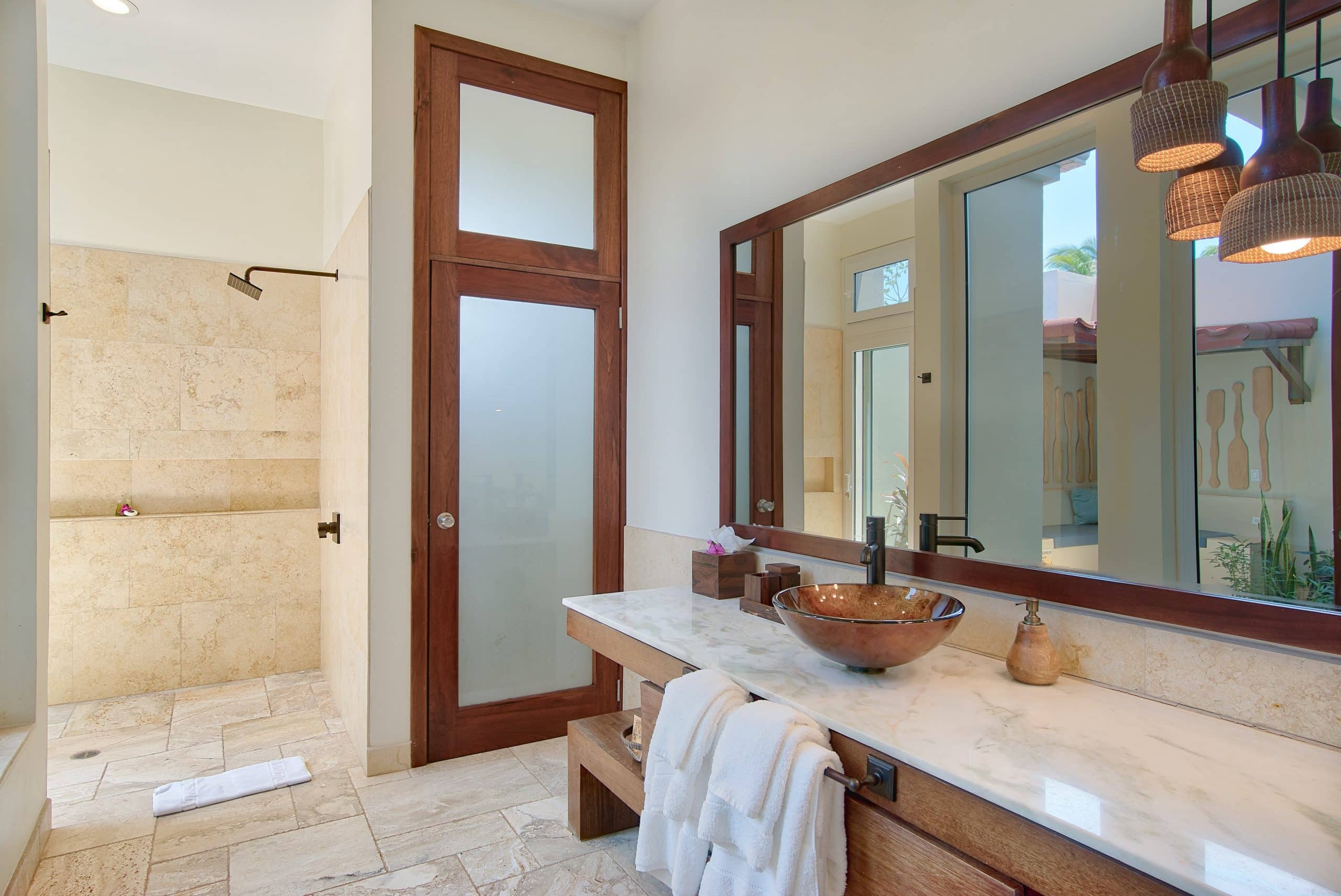 Bathroom with shower, large vanity mirror, white counter and ceramic sink inside of the Deluxe Suite Lower Level with Plunge Pool at The Lodge at Jaguar Reef Resort