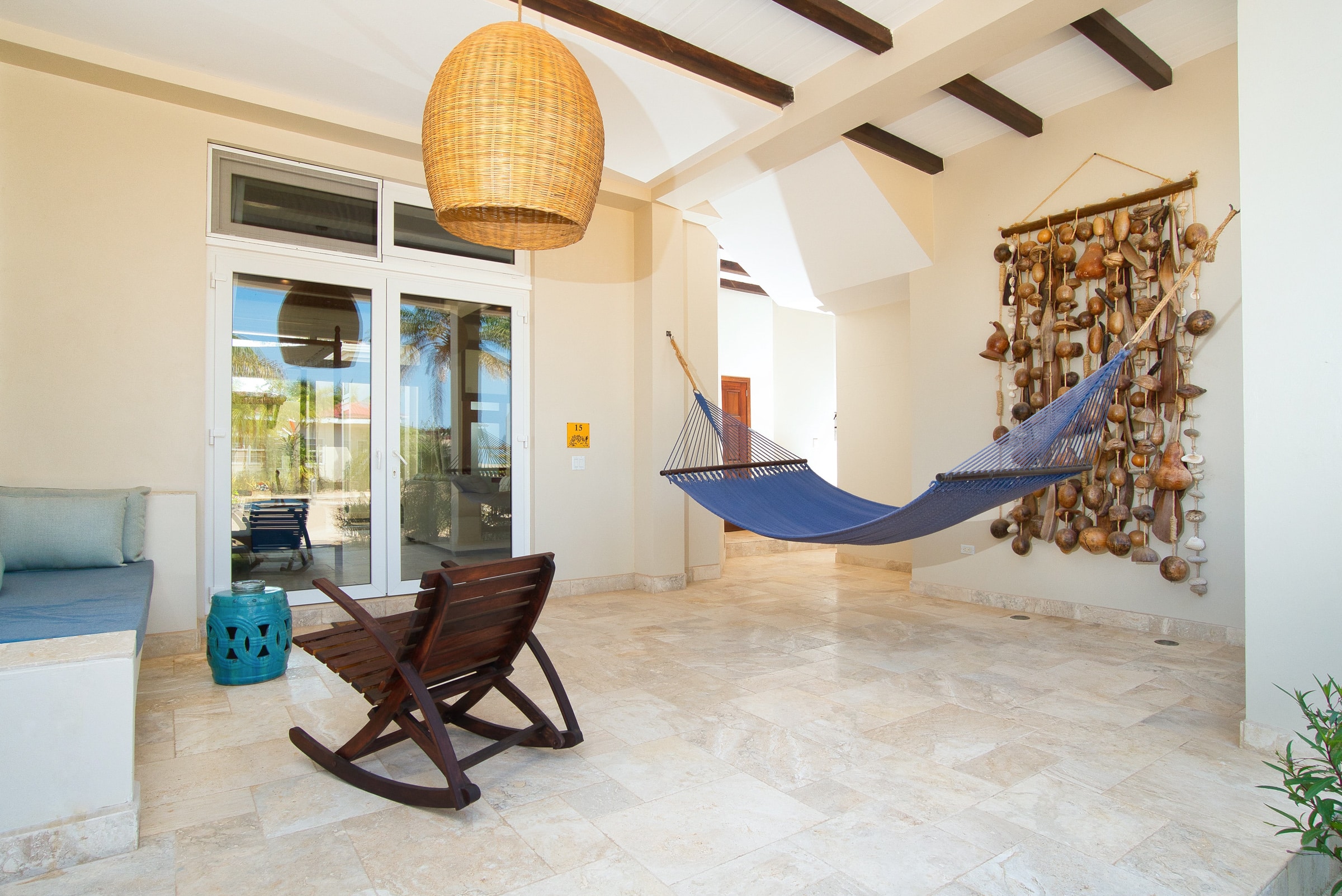 Front patio with cement bench, wooden rocking chair and a blue swinging hammock outside of the Deluxe Suite Lower Level with Plunge Pool at The Lodge at Jaguar Reef Resort