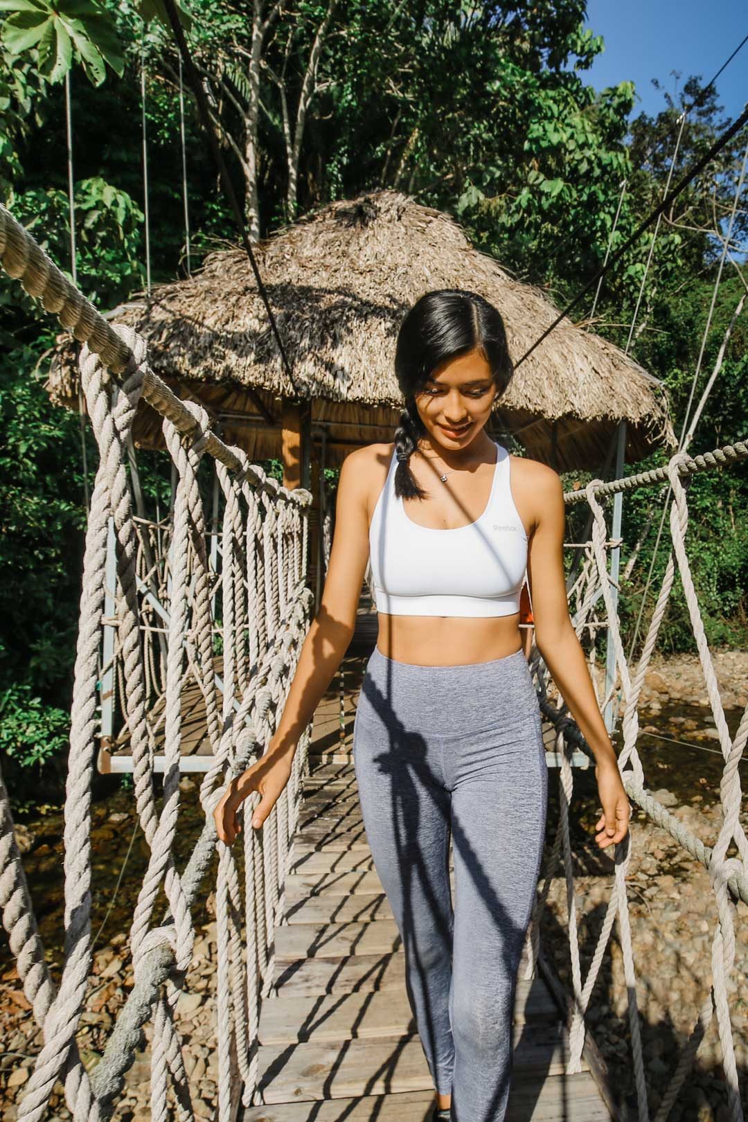 Gest standing on a swinging rope bridge with a thatched structure in the background